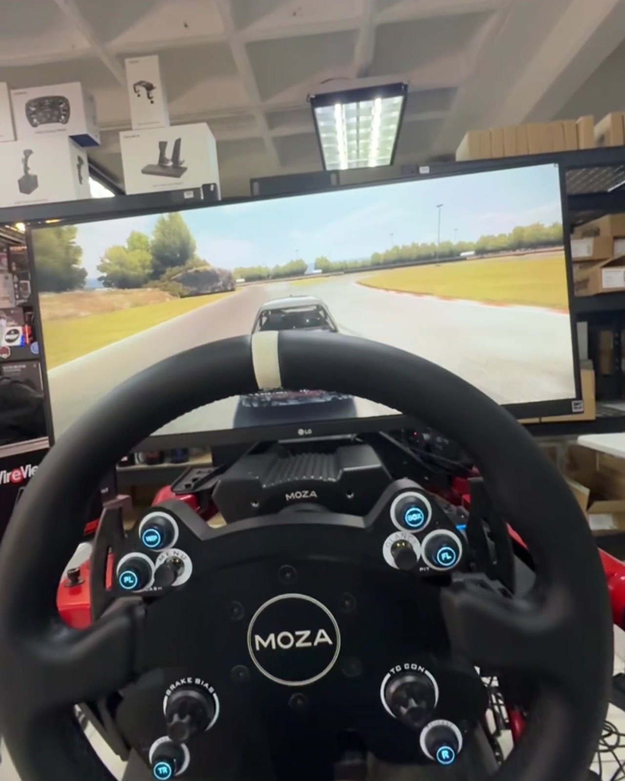 Volante circular de Moza en un simulador de carreras de Quantum Imports, con una pantalla de carrera al fondo.