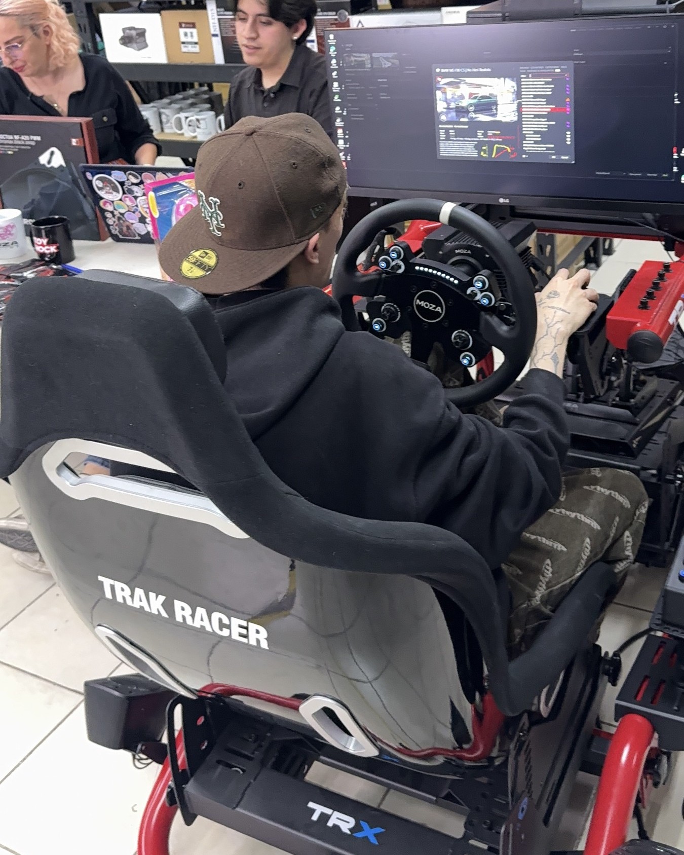 Bryan, con gorra, sentado en un simulador Trak Racer en las oficinas de Quantum Imports.