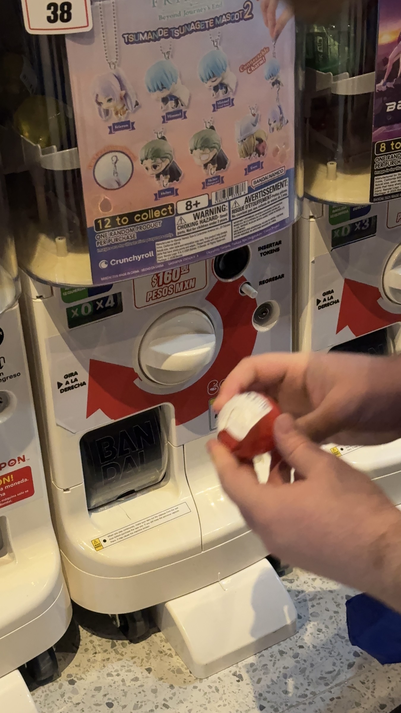 Manos abriendo una cápsula de gashapon frente a una máquina de Bandai en la tienda de Bandai Namco.