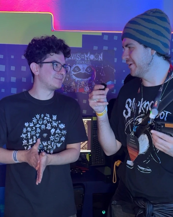 David Tapia junto a Juan Pablo, de Amano, frente al póster de Devils on the Moon Pinball en el Banamex Super Indie Games 2026.