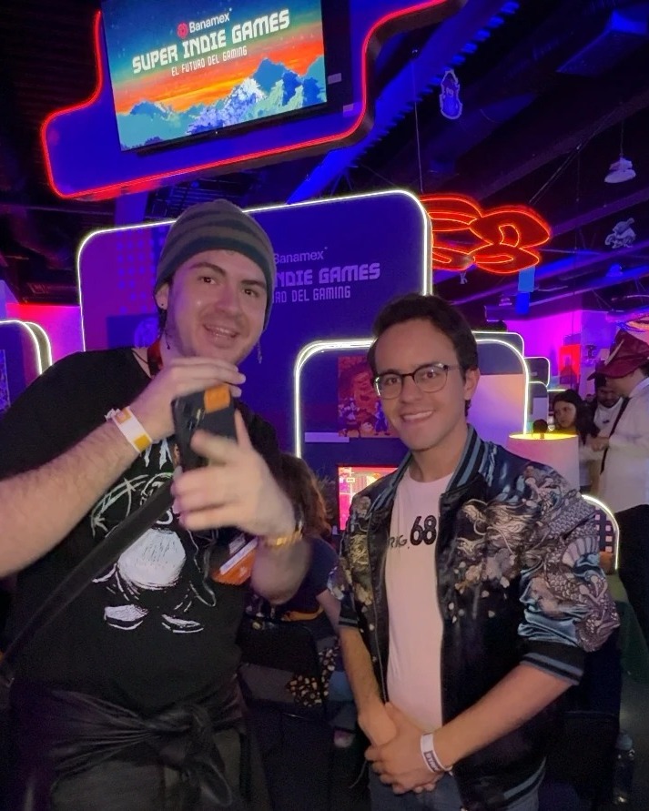 David Tapia junto a uno de los desarrolladores de The Pumpkin Paradox frente al letrero del Banamex Super Indie Games 2026.